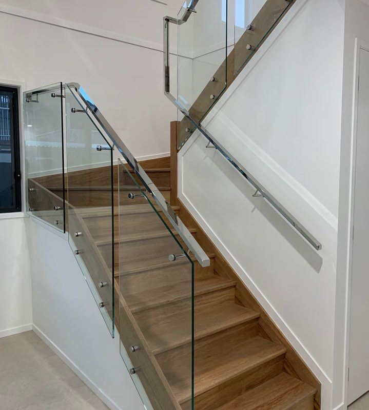 Stylish staircase with wooden steps, glass balustrades, and sleek stainless steel handrails, creating a contemporary and open-concept interior design.