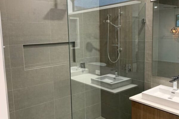 Modern bathroom with a frameless glass shower, large overhead rain shower, and gray tile walls. Floating vanity with a white countertop and under-sink storage enhances the clean, contemporary aesthetic