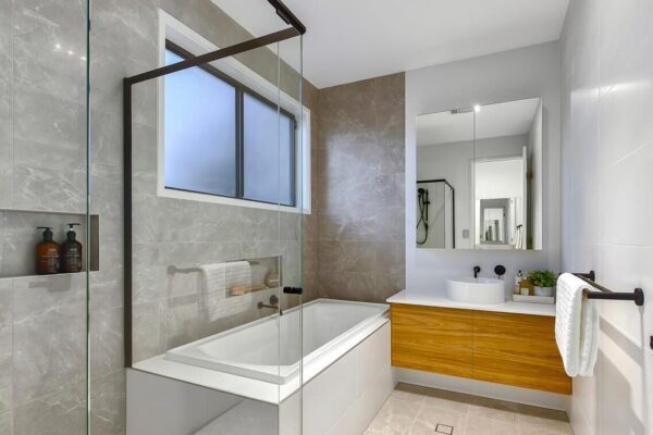 Luxury bathroom featuring a sleek glass shower screen, built-in bathtub, wood vanity, and elegant marble-look tiles for a contemporary design.