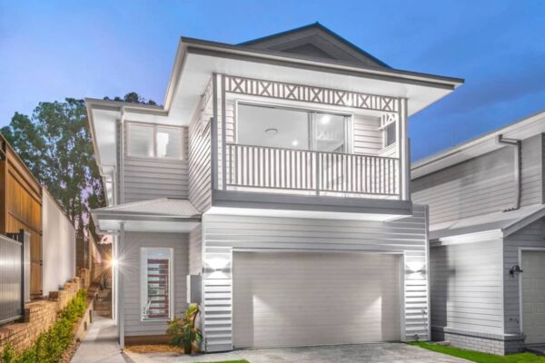 Modern two-story custom-built home with a Hamptons-style façade, featuring a spacious balcony, white timber finishes, and a well-lit exterior at dusk.