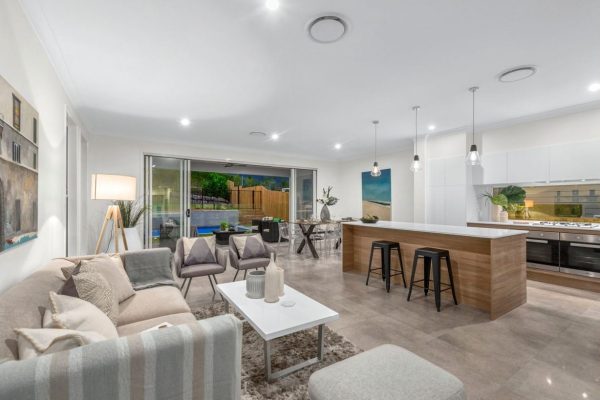 Stylish open-plan kitchen renovation by Jensen Constructions Qld, featuring a modern island with wood paneling, pendant lighting, and sleek white cabinetry, seamlessly connected to the living area and outdoor patio.