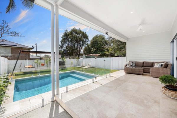 Contemporary home extension featuring an elegant patio, glass pool fencing, and a spacious seating area. Jensen Constructions enhances Brisbane homes with seamless indoor-outdoor designs.