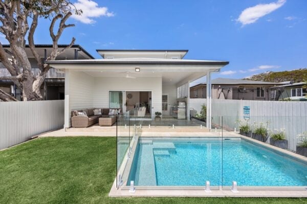 Modern backyard renovation in Brisbane featuring a luxurious pool, glass fencing, and covered alfresco area. Designed and built by Jensen Constructions for seamless indoor-outdoor living.