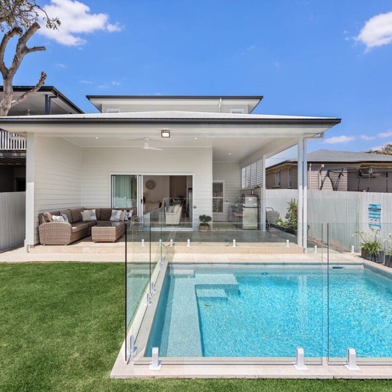 Modern backyard renovation in Brisbane featuring a luxurious pool, glass fencing, and covered alfresco area. Designed and built by Jensen Constructions for seamless indoor-outdoor living.