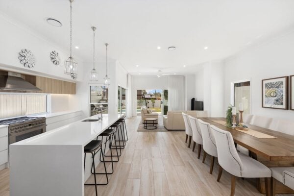 Spacious open-plan kitchen, dining, and living area with a sleek white island, pendant lighting, and natural wood accents. Designed by Jensen Constructions, Brisbane’s experts in high-end home renovations.