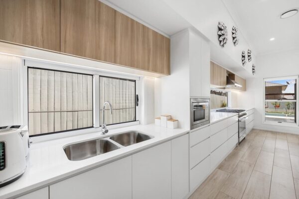 Contemporary kitchen renovation in Brisbane featuring sleek white cabinetry, wood-accented overhead cupboards, and a spacious galley layout. Designed by Jensen Constructions for a stylish and functional home.