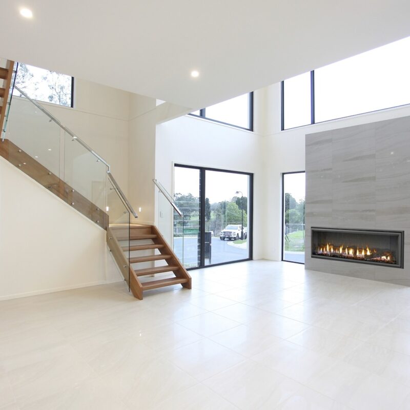 Luxury home renovation in Brisbane by Jensen Constructions. Featuring a stunning open-plan living space, modern fireplace, floating timber staircase with glass balustrade, and floor-to-ceiling windows for natural light.
